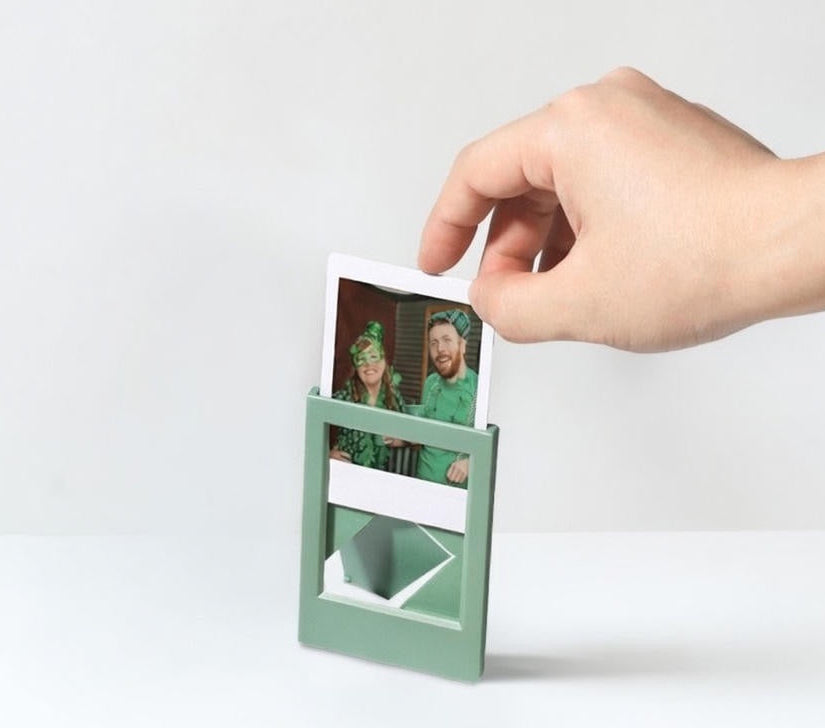 Hand holding a small green photo frame with a printed photo inside on a white background