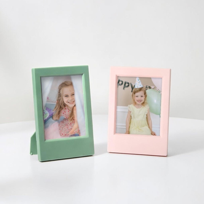 Two pastel-colored mini picture frames with photos of children on a white surface.